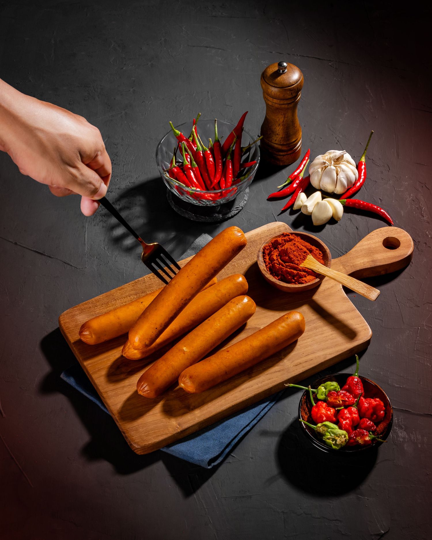 Hot dogs on wooden cutting board with red chili peppers and garlic for seasoning.