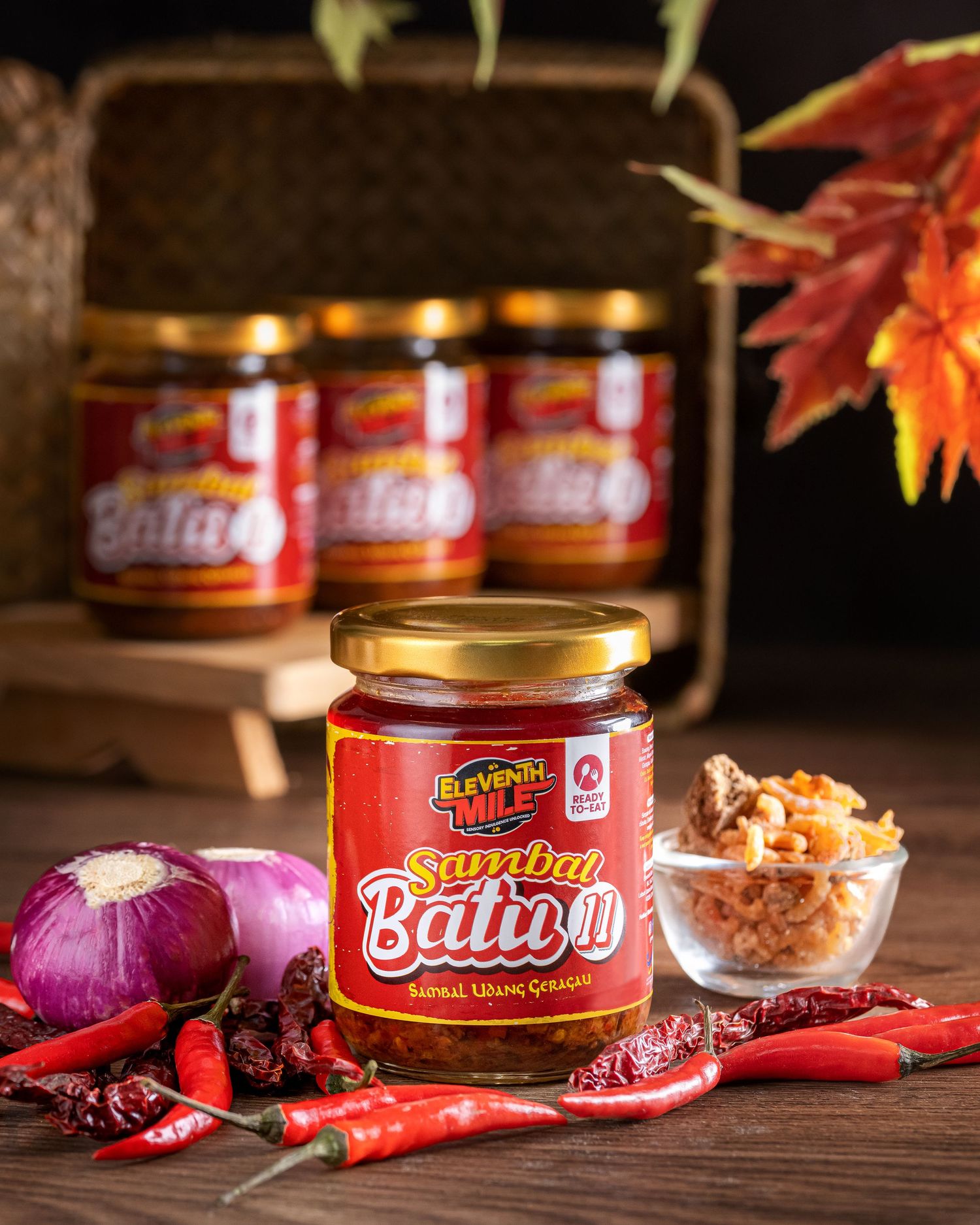 Jars of spicy sauce with red chilies and purple onions on wooden background.
