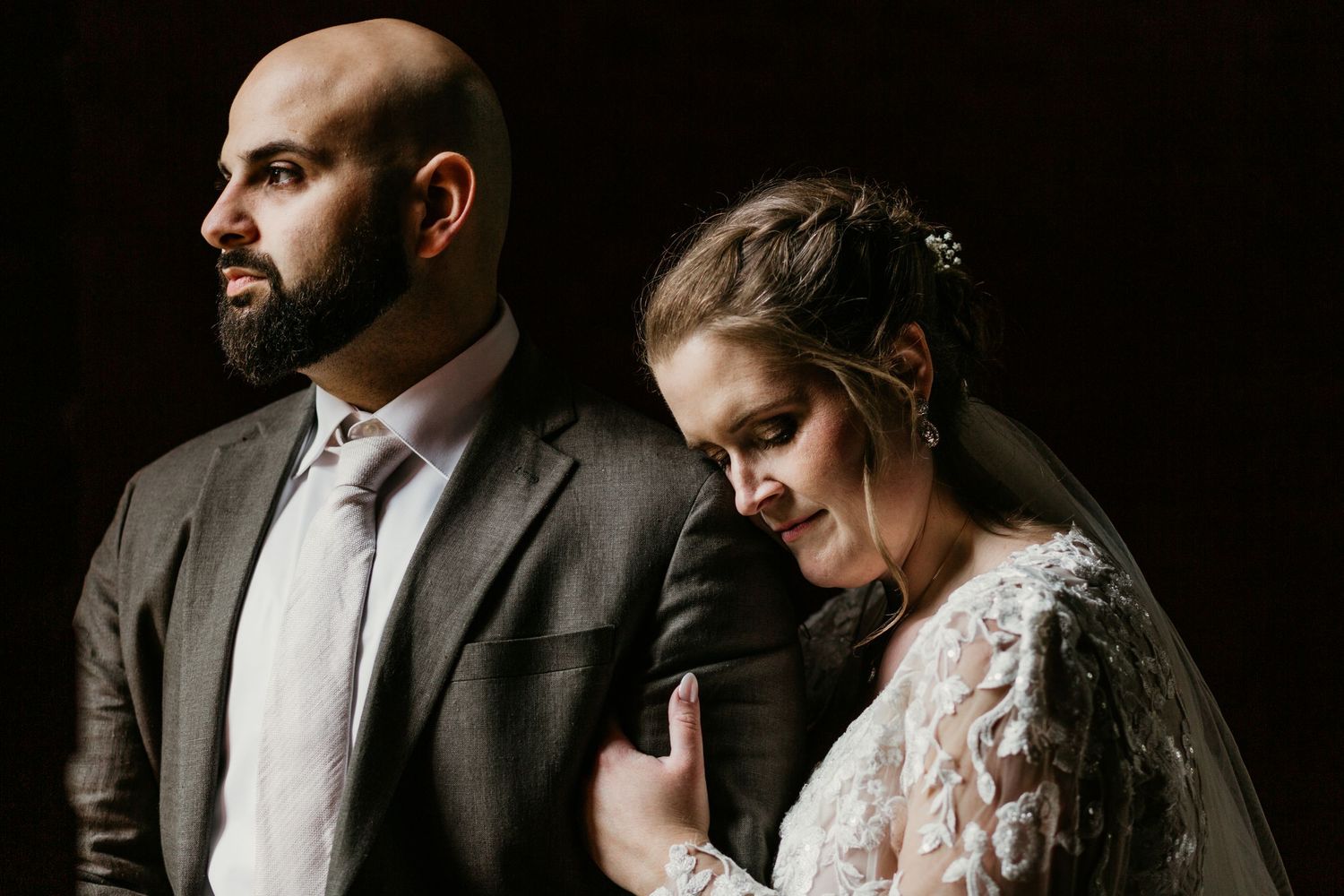 Intimate wedding portrait showing couple in formal attire against dark background.