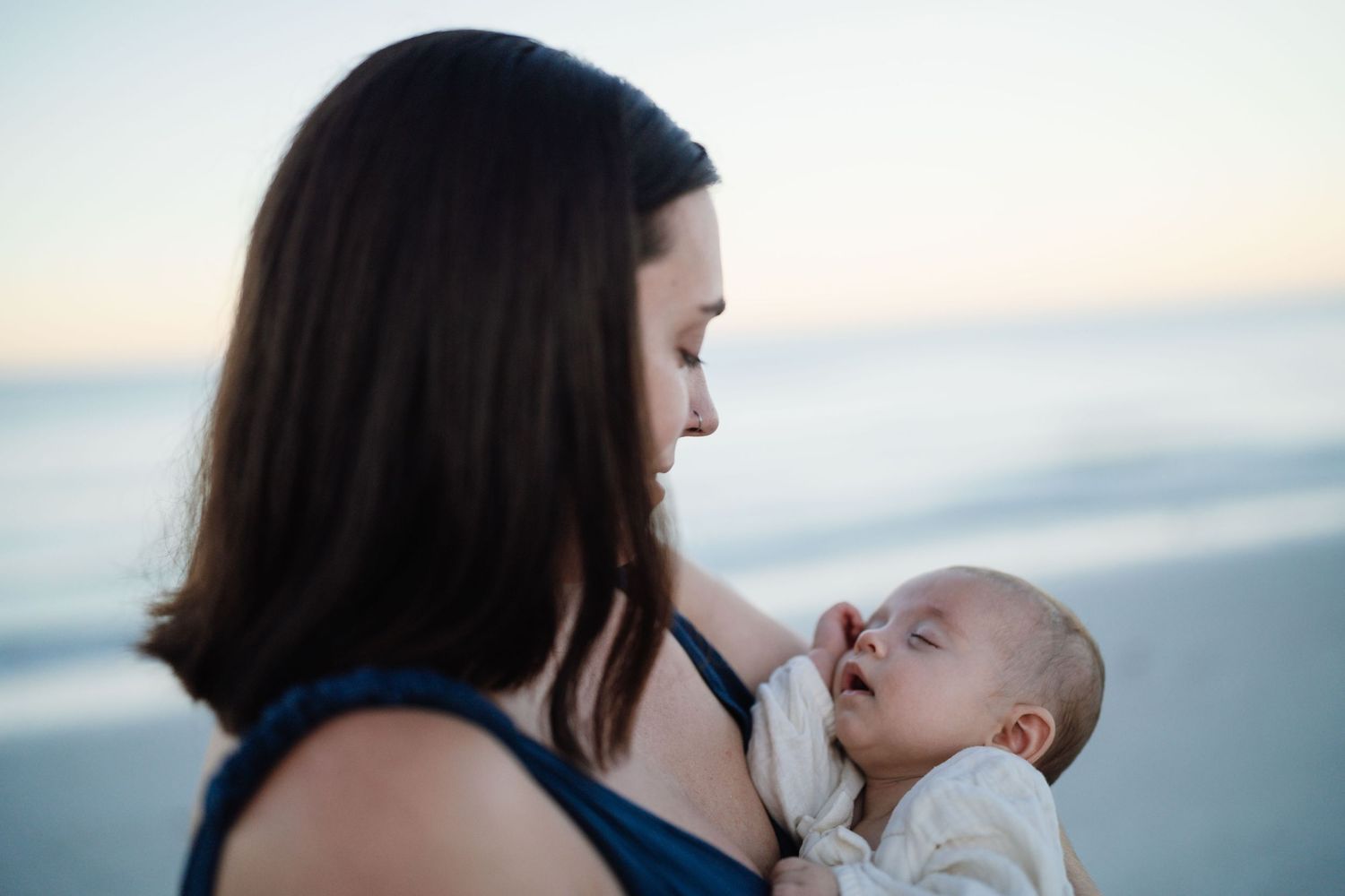 A tender moment between parent and infant against a serene beach backdrop at sunset.