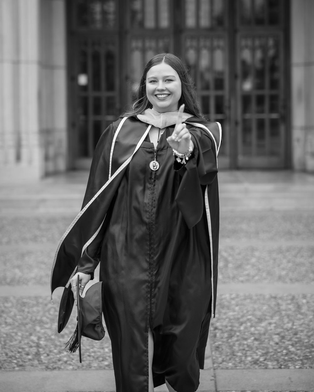 Woman in doctoral graduation gown and cap smiling and posing outdoors in black and white photo.