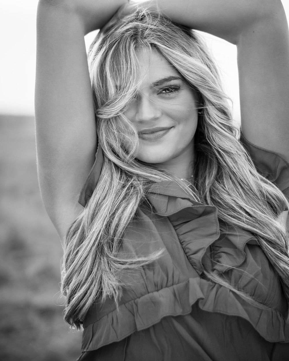 Black and white portrait of a smiling woman with long flowing blonde hair wearing a ruffled top.