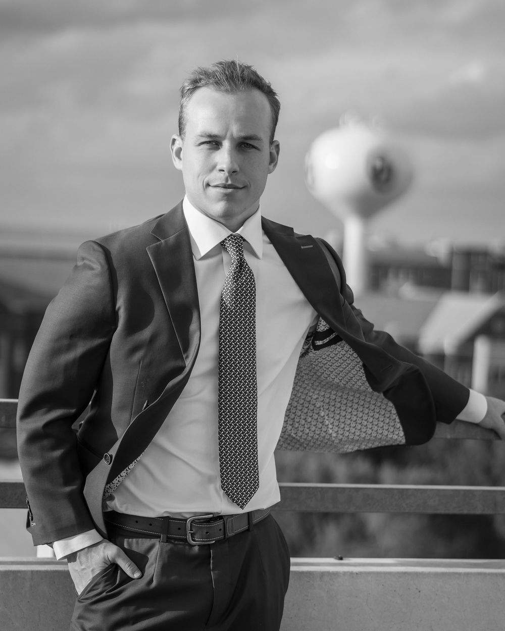 Black and white portrait of a confident businessman in suit and tie posing outdoors on a rooftop.