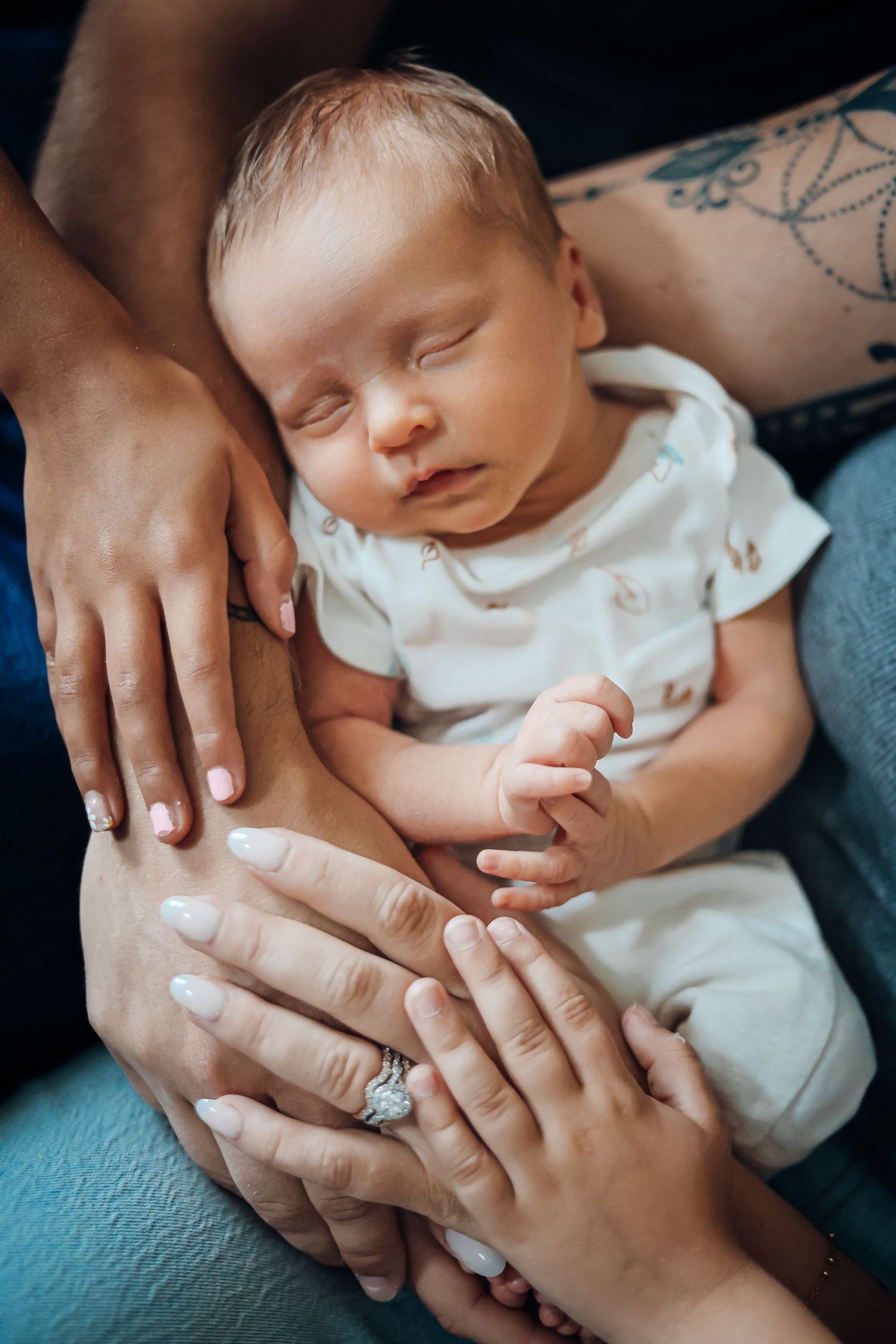 Gentle hands cradling sleeping newborn baby in white onesie. Example of family style newborn photography sessions