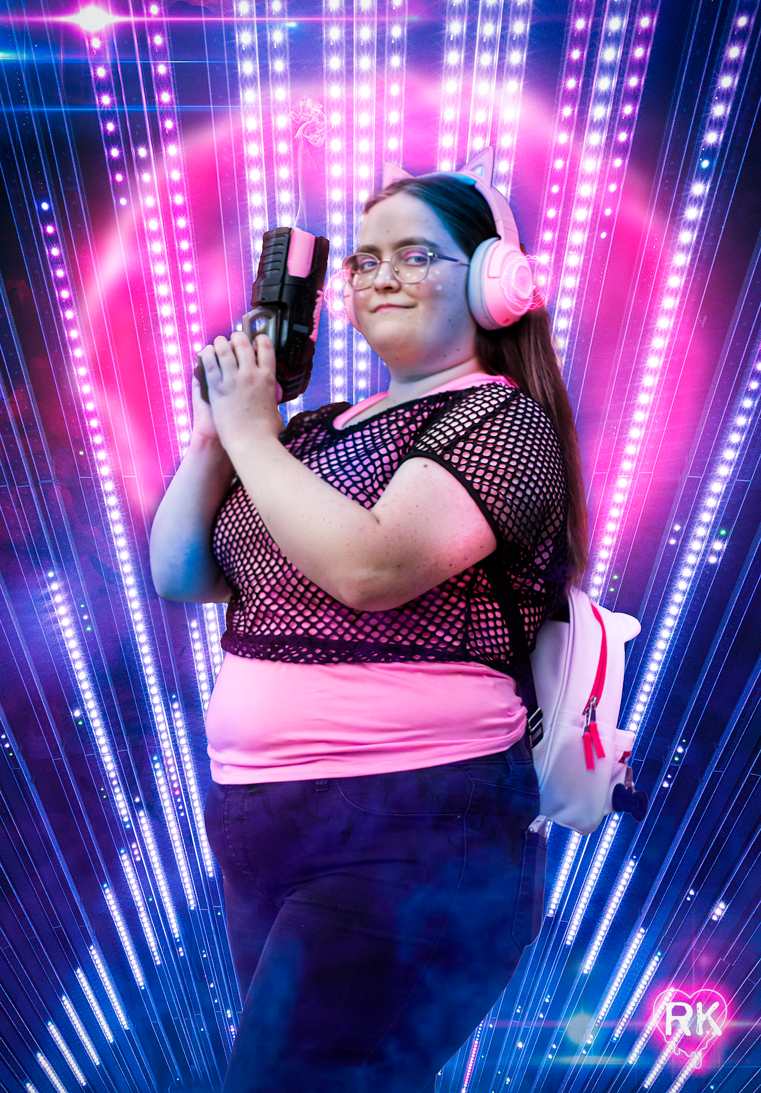 Gamer with pink headphones and mesh top poses with toy gun against neon light background.
