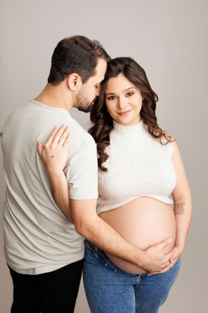 Intimate maternity portrait of couple in casual attire against light background.