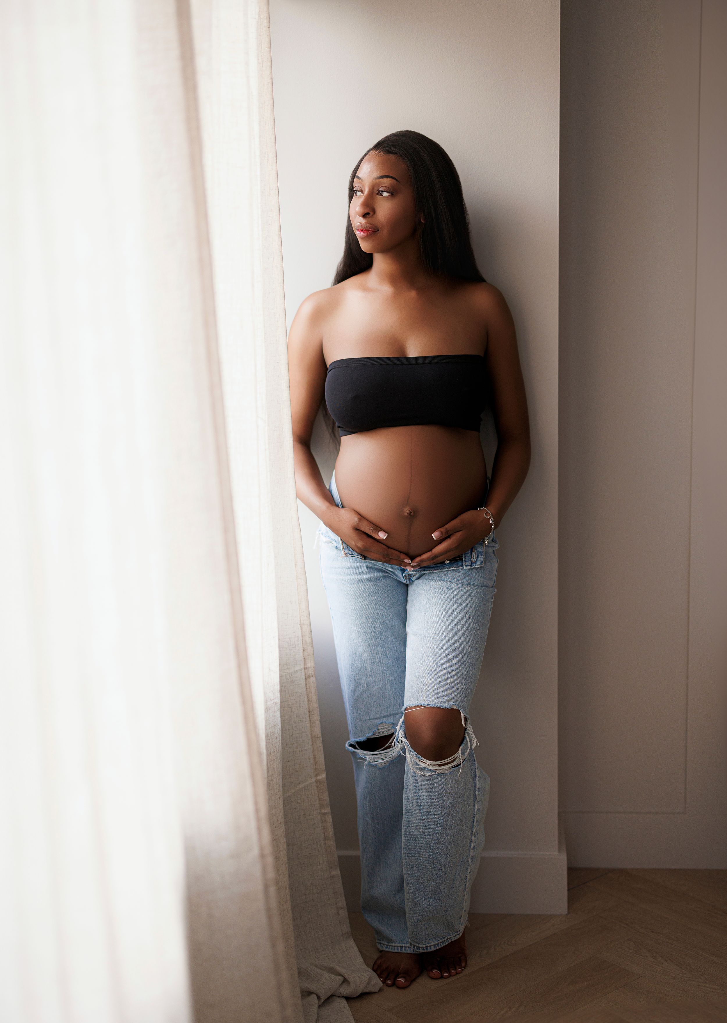 A series of artistic maternity photos showing a woman in ripped jeans and black top against a light background.