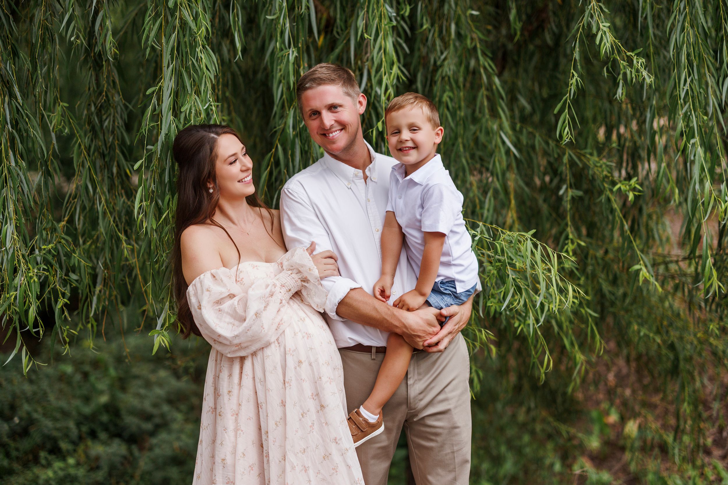 A family shares a joyful moment together under the drooping branches of a willow tree on a sunny day.