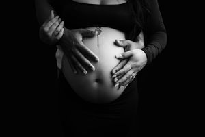Image of a pregnant belly with mom and dad's hands holding belly.  Image is black and white.