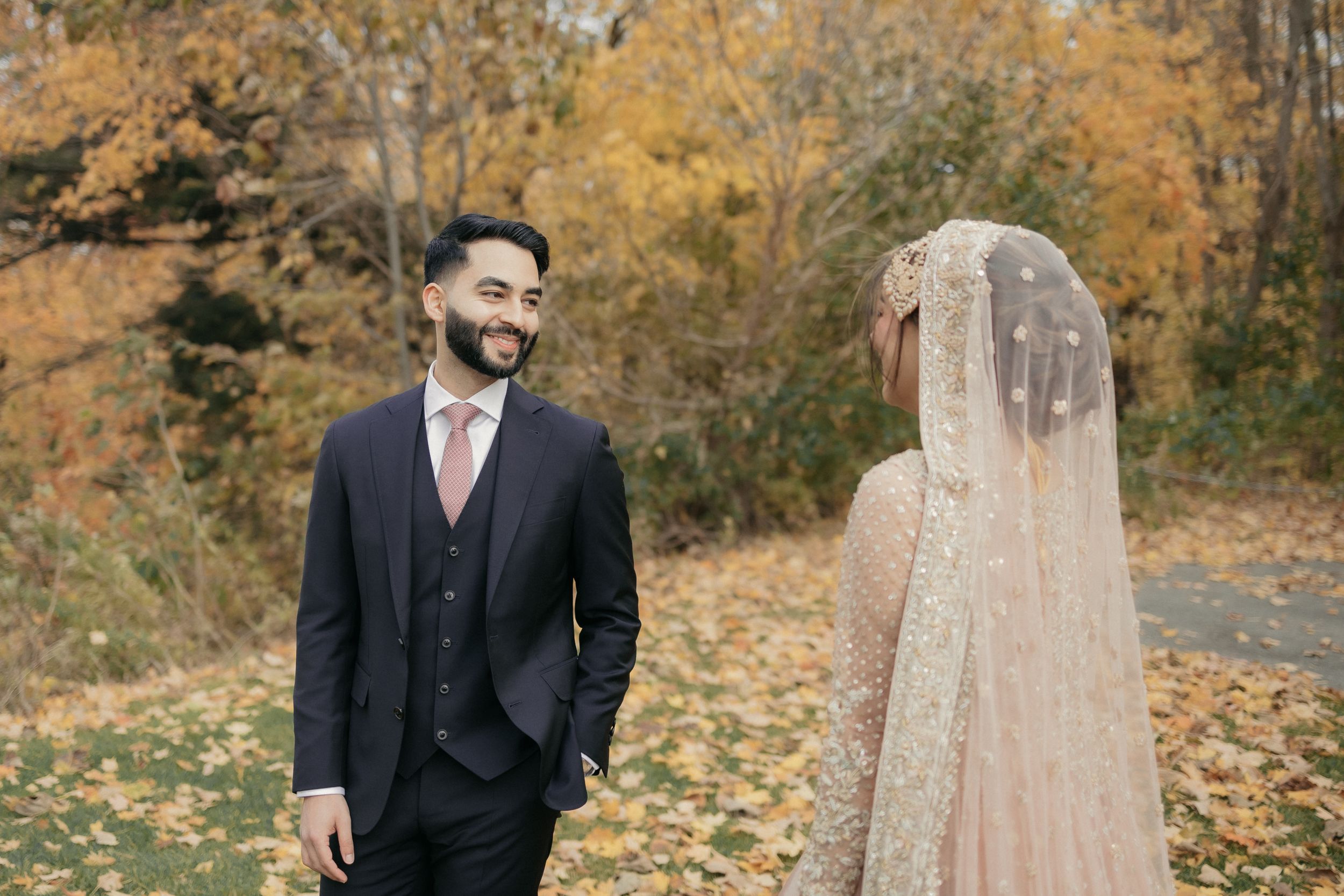 Bride in champagne veil and groom share moment in fall foliage setting.