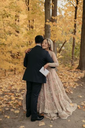 Newlyweds embrace in intimate moment surrounded by golden fall foliage.