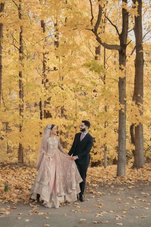 Couple walking together through a forest with golden autumn foliage wearing traditional wedding attire.