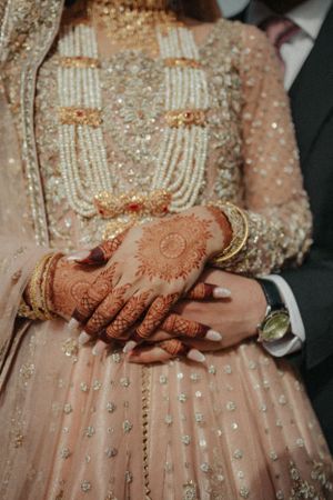 Close-up of hands with henna and jewelry details on blush pink embellished wedding dress.