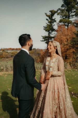 Couple sharing a joyful moment outdoors with autumn trees in background wearing wedding attire.