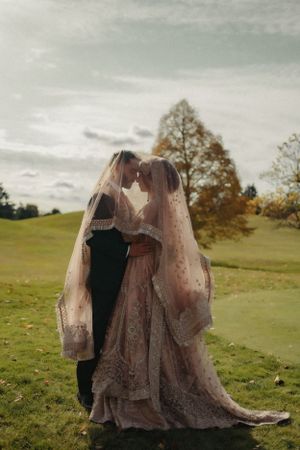 Wedding couple embracing under sheer veil in outdoor meadow with autumn scenery.
