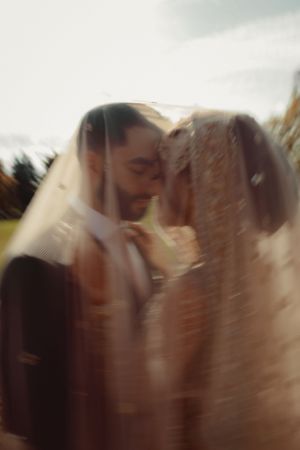 Artistic blurred photo of couple sharing intimate moment under wedding veil.