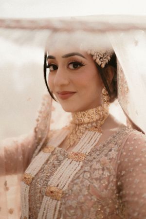 Portrait of bride wearing intricately detailed blush pink wedding dress and veil.