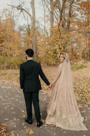 A romantic autumn wedding photo showing a couple in a dress and suit walking among fallen leaves.