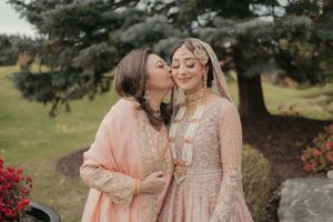 Tender moment captured between bride and companion in soft peach and blush tones outdoors.
