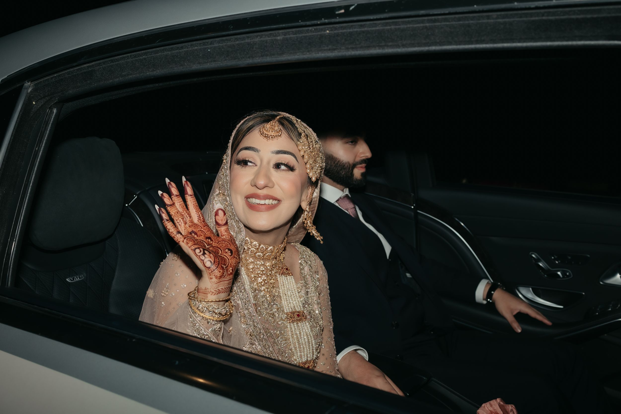 Bride adorned in traditional henna and jewelry smiles from car window.