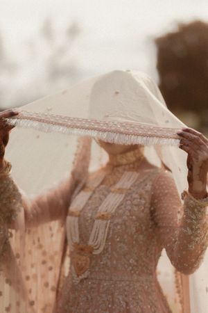 Delicate lace veil being adjusted on bride in traditional South Asian wedding attire.