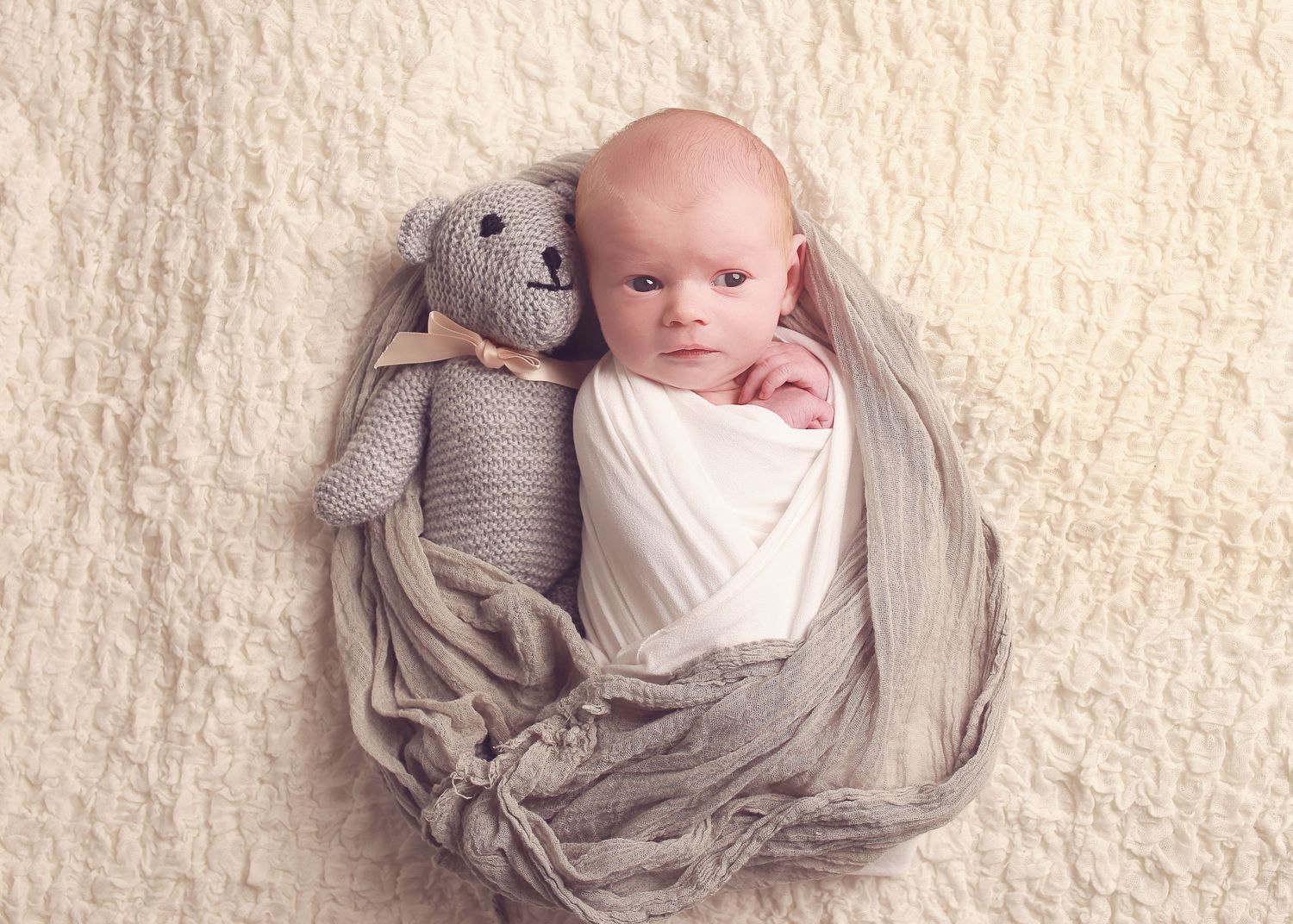 A sweet newborn cuddled up with a soft teddy bear, capturing the innocence and warmth of early life in a peaceful newborn photography sessio