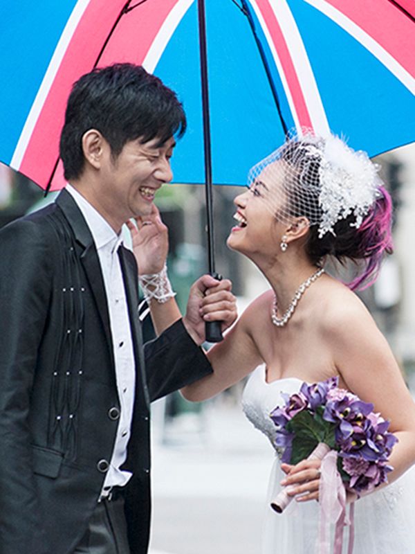 A Japanese couple stands under a Union Jack umbrella, showcasing their love during a wedding at Abigail's Studio in High Wycombe.