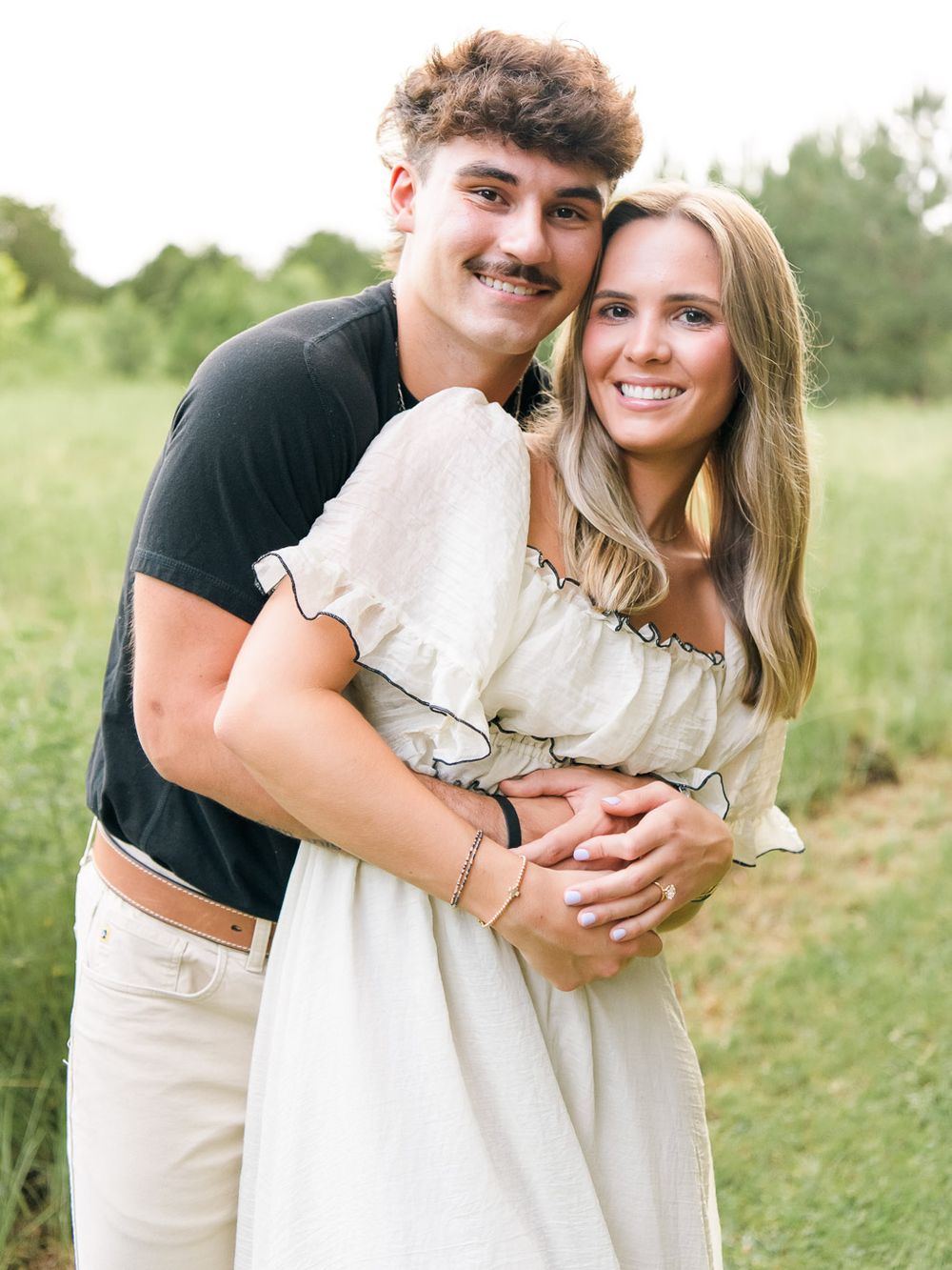 Romantic couple embracing in a sunny outdoor field wearing light colored clothing.