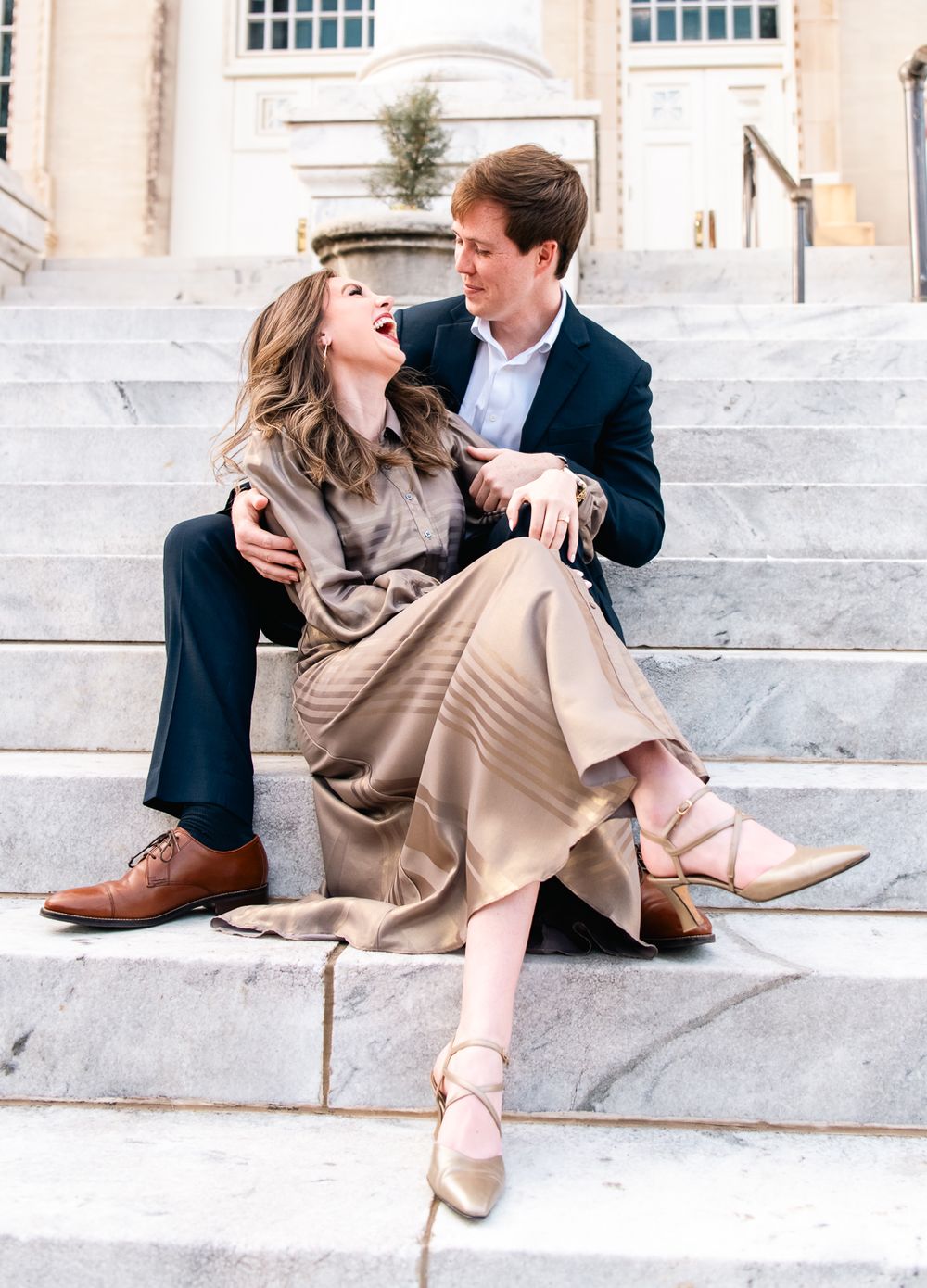 A joyful couple sharing a laugh while sitting on white stone steps.