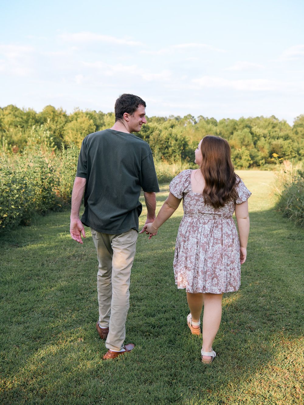 Couple walks hand in hand through a sunny meadow path on a summer afternoon.
