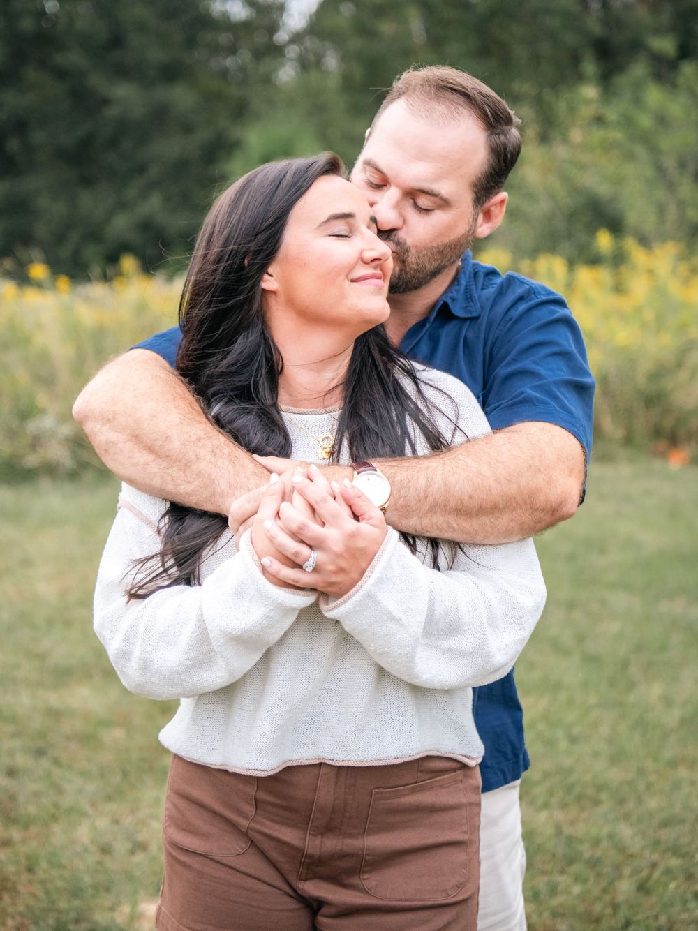 Candid moment of a couple laughing and embracing in a sunny field.