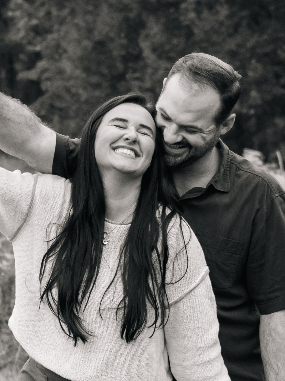 Black and white portrait of a couple sharing joyful laughter together outdoors.