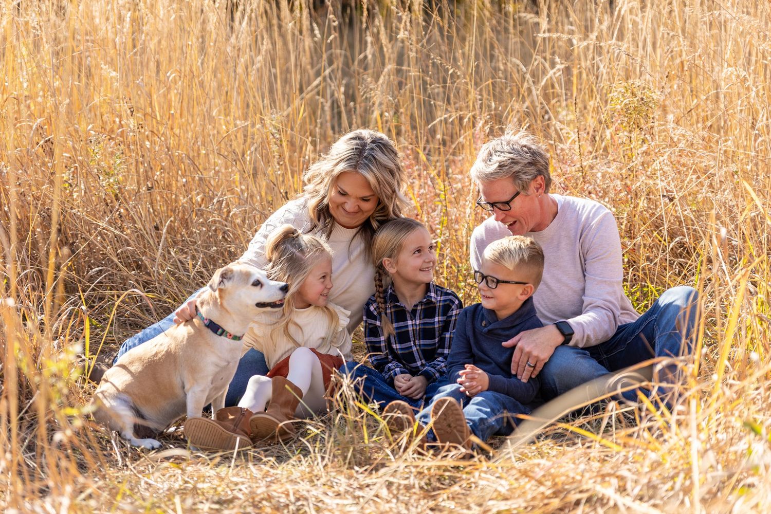 Happy family with two children and a golden dog sitting together in a golden autumn wheat field.
