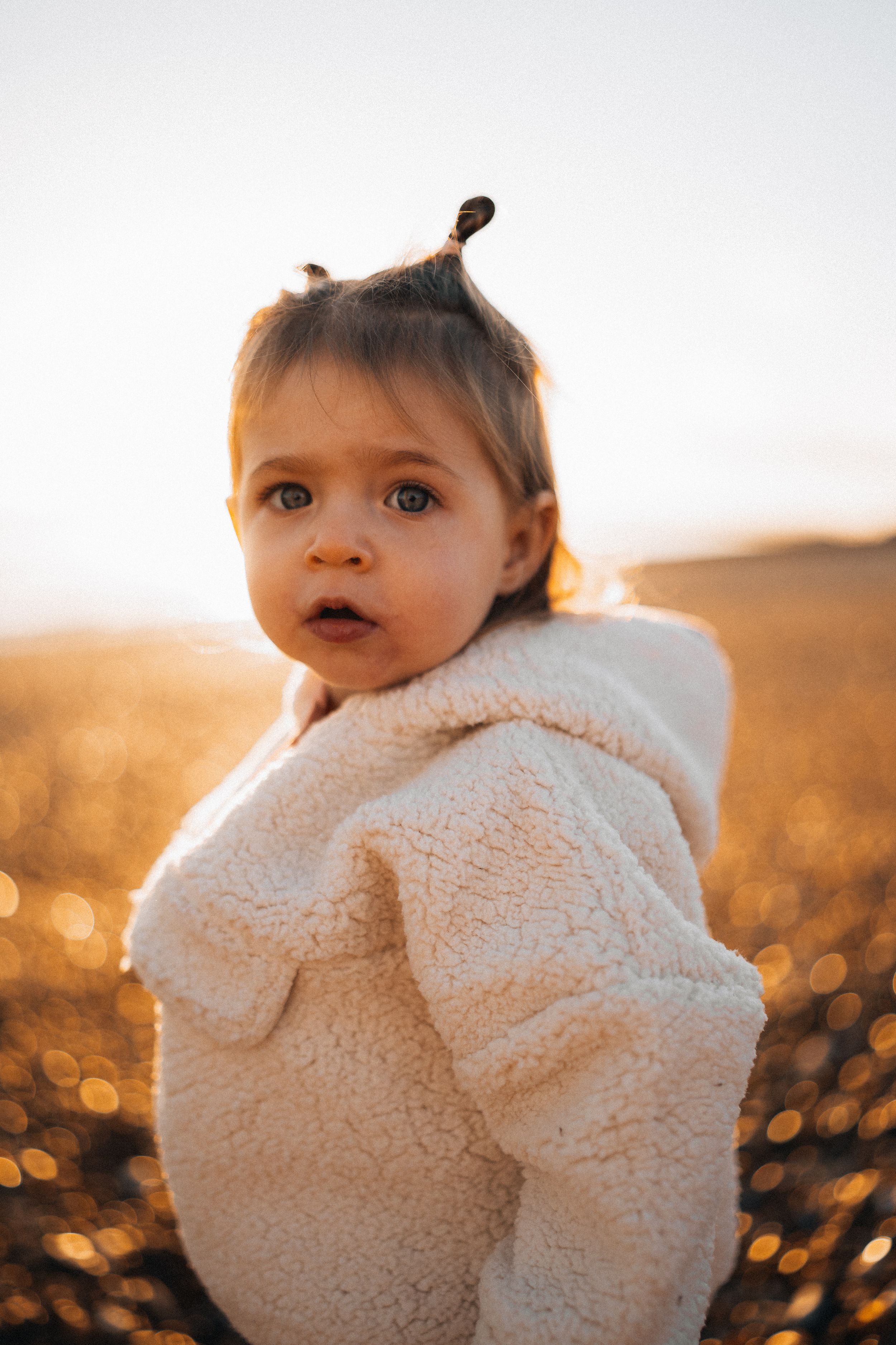 Child wearing cozy white fleece jacket in golden sunset light.