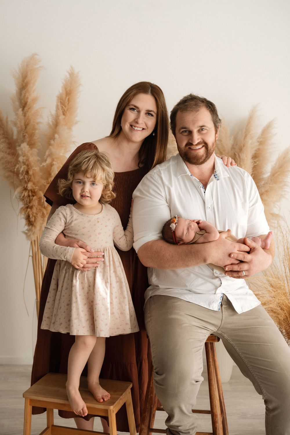 Family portrait with parents and two children, newborn baby, toddler girl, pampas grass decor, studio photography.