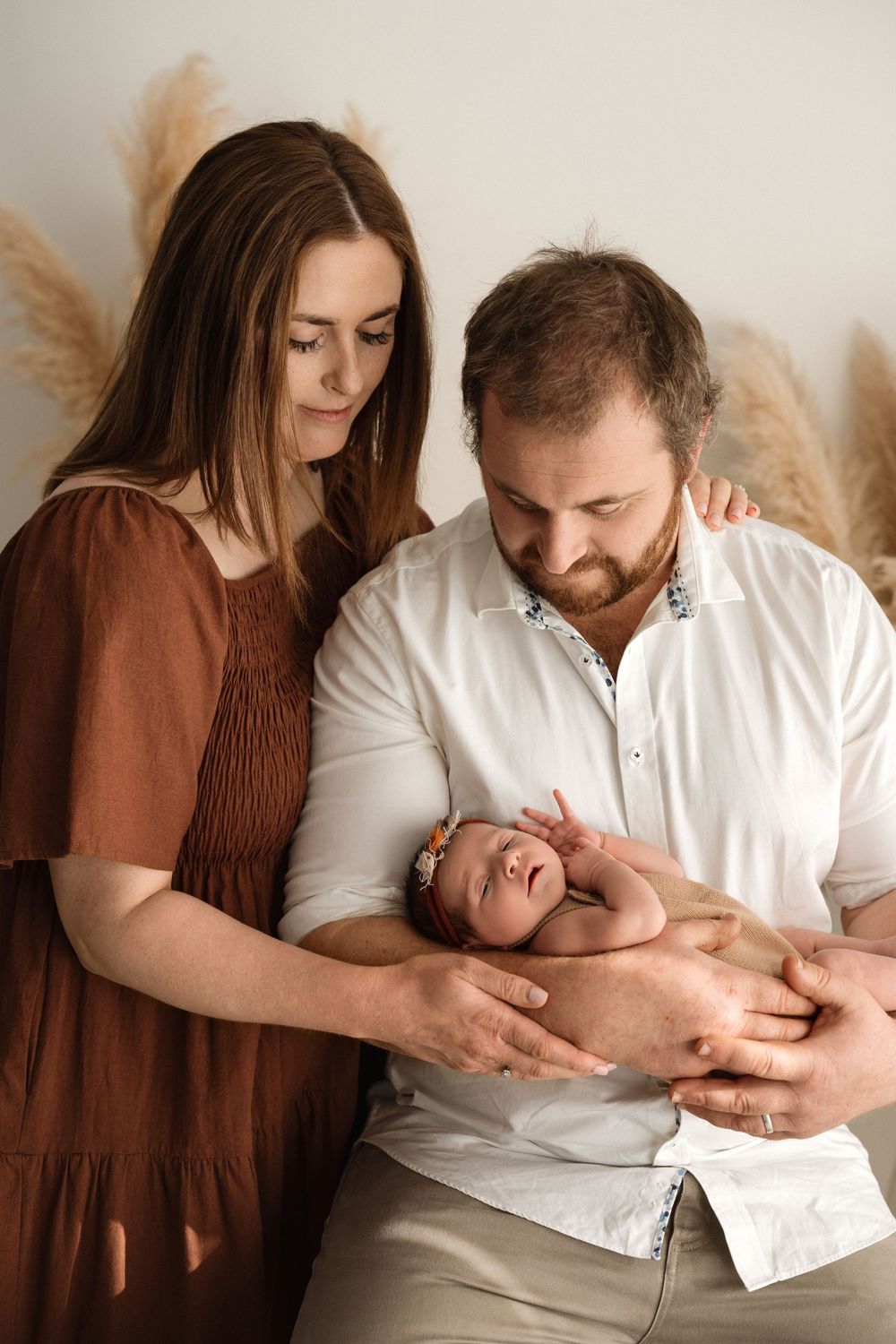 A couple tenderly holds their sleeping newborn baby during a professional family portrait session with boho decor.