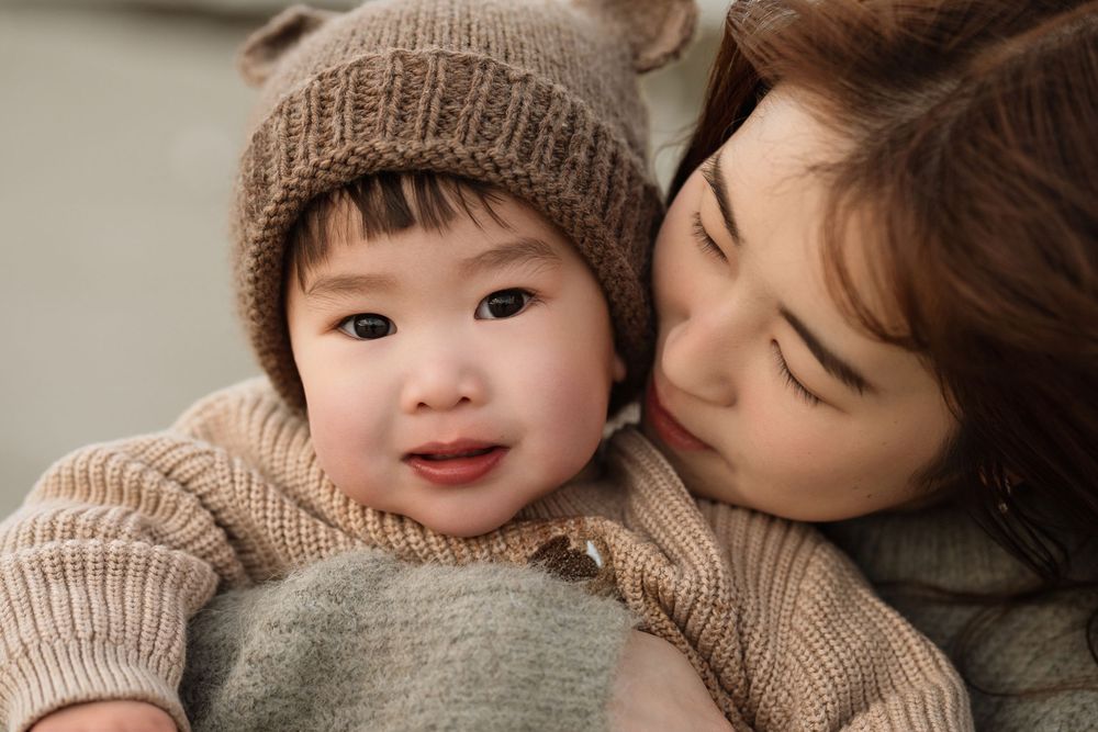 A mother tenderly holds her baby wearing a knit bear hat and sweater, sharing a warm and loving moment.