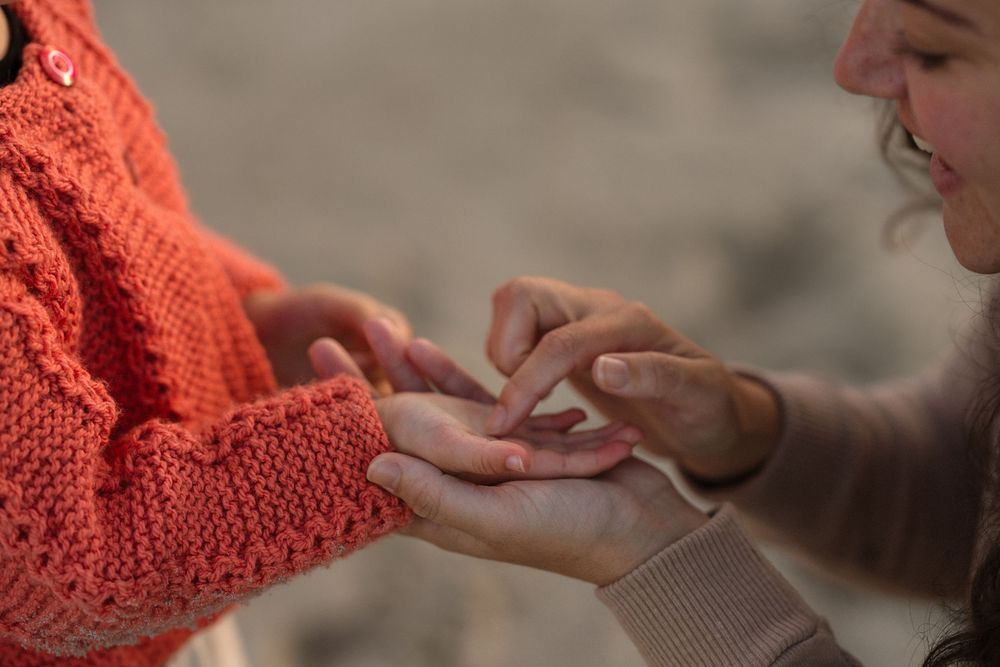 Close-up of two people gently holding hands outdoors, one wearing an orange knit sweater, sharing a tender moment.