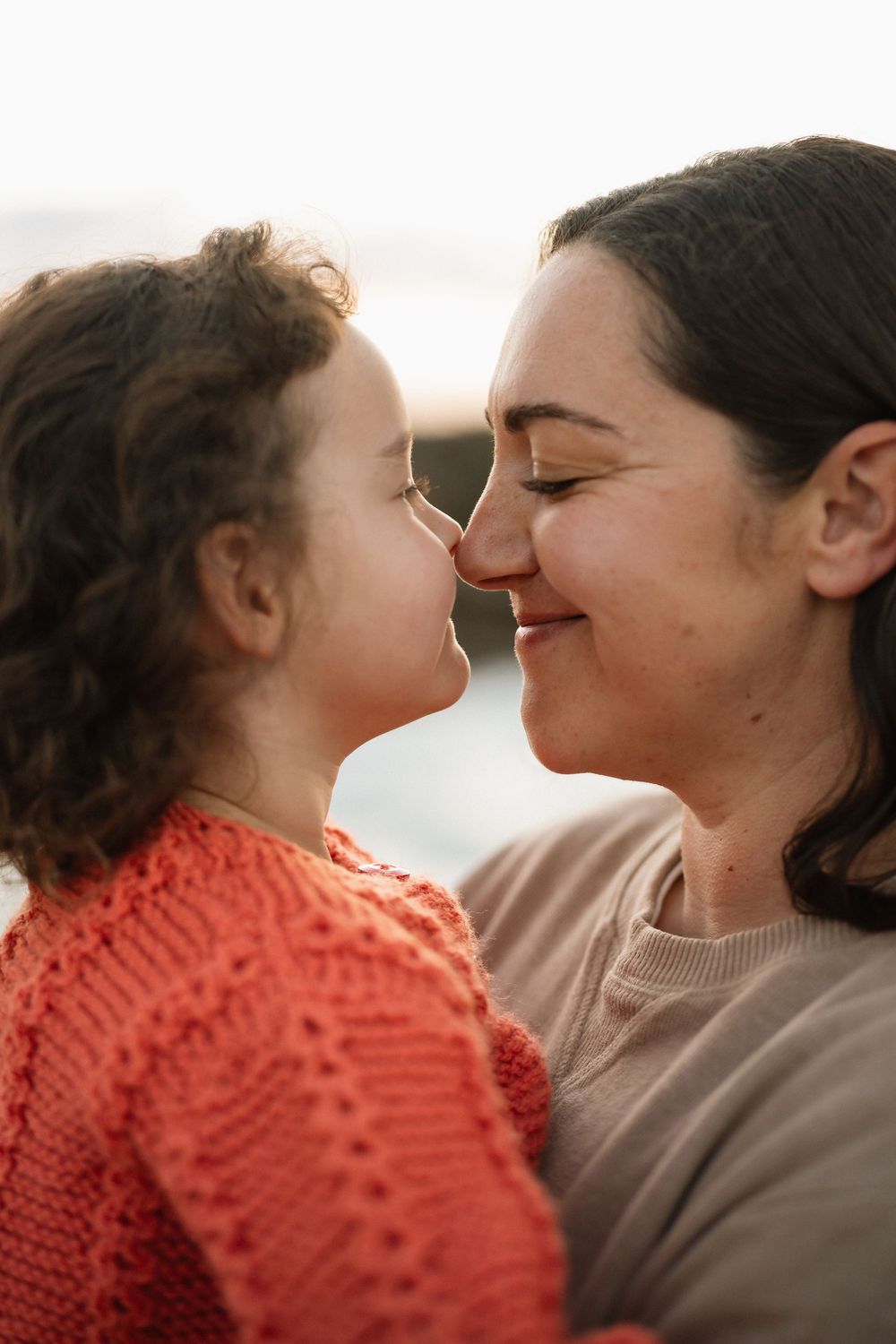 A mother and young child share a tender nose-to-nose moment, smiling warmly in soft natural light.