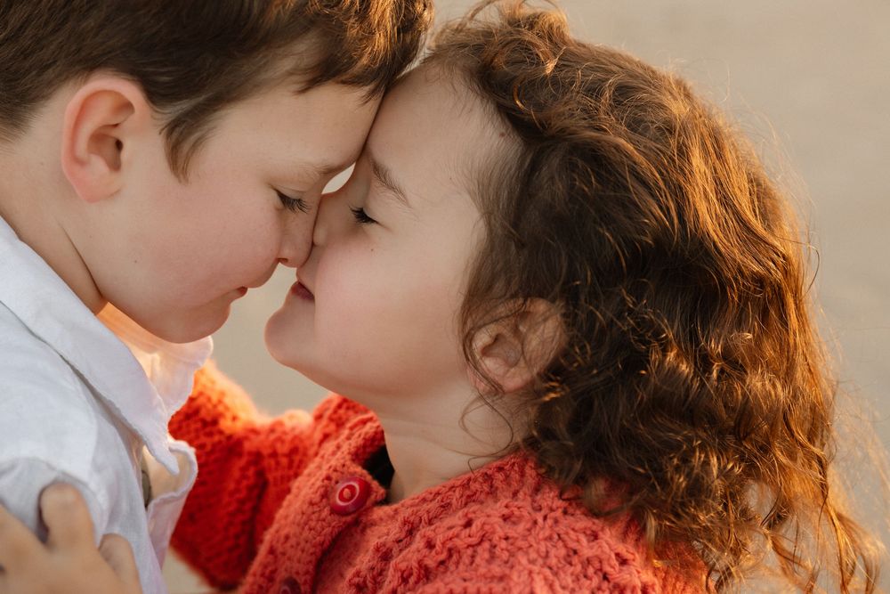 Two young siblings touching foreheads in a tender, loving moment outdoors.