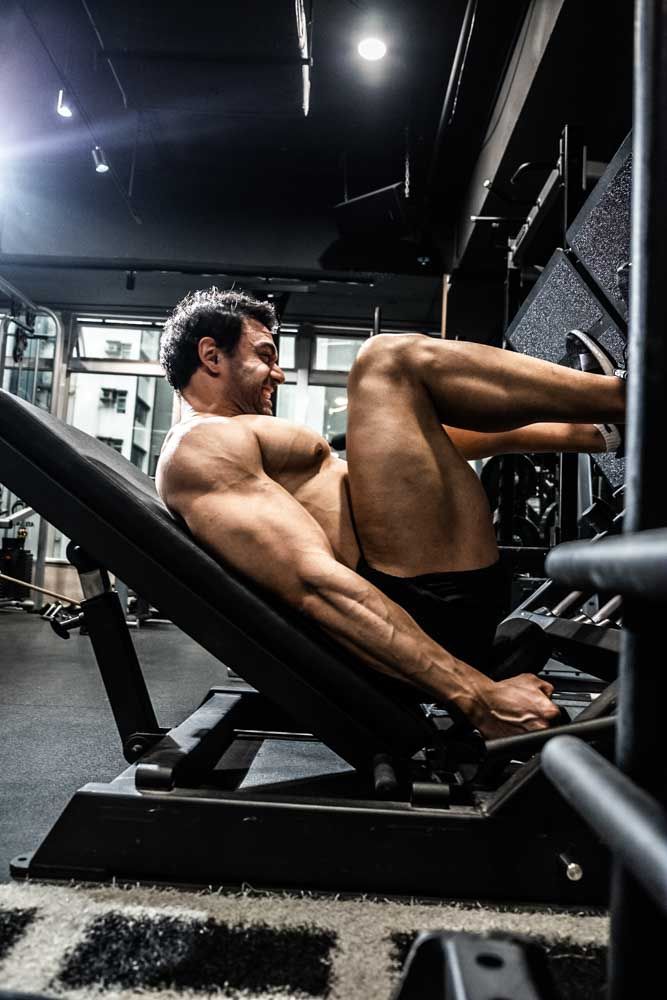 Muscular man performing leg press exercise on gym machine, showcasing defined physique in dark fitness center.