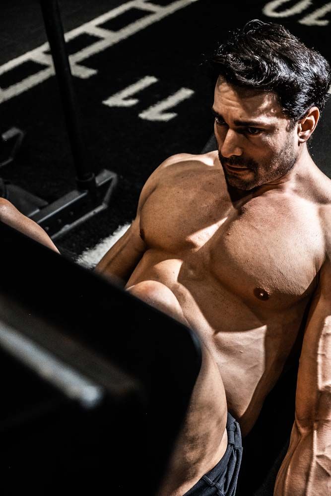 Muscular shirtless man exercising in gym with dramatic lighting highlighting his defined physique and strong arms.
