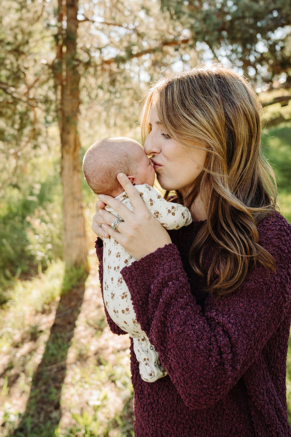 Intimate bonding moment outdoors with baby in burgundy sweater.