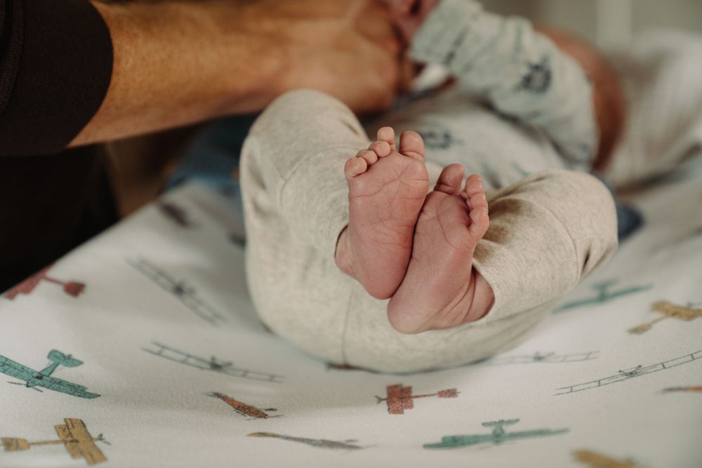Tiny baby feet peek out from beneath a patterned blanket with airplanes and geometric shapes.