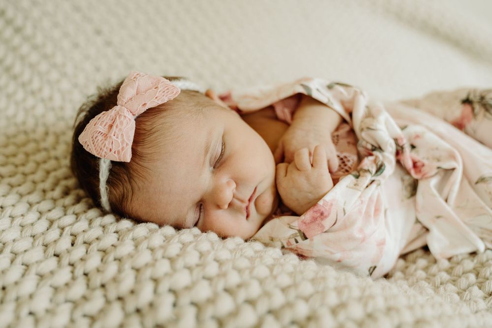 Peaceful sleeping newborn in pink wearing a bow headband on cream knit blanket.