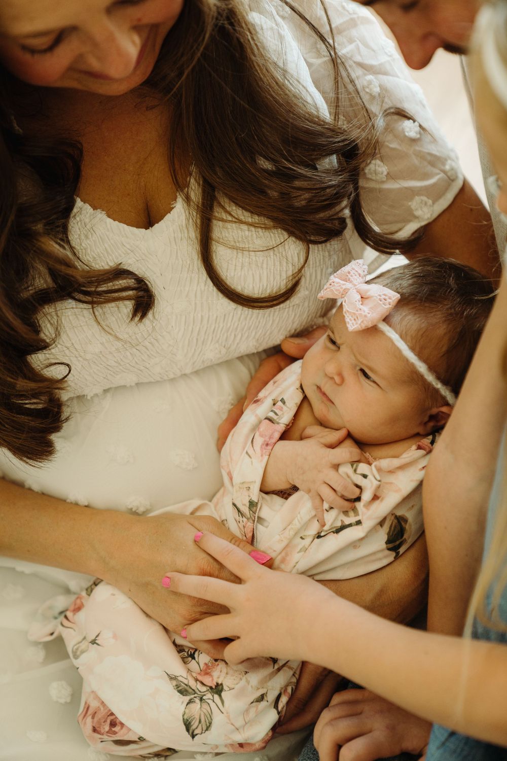 Close up of a sleeping newborn in a floral outfit surrounded by loving family.