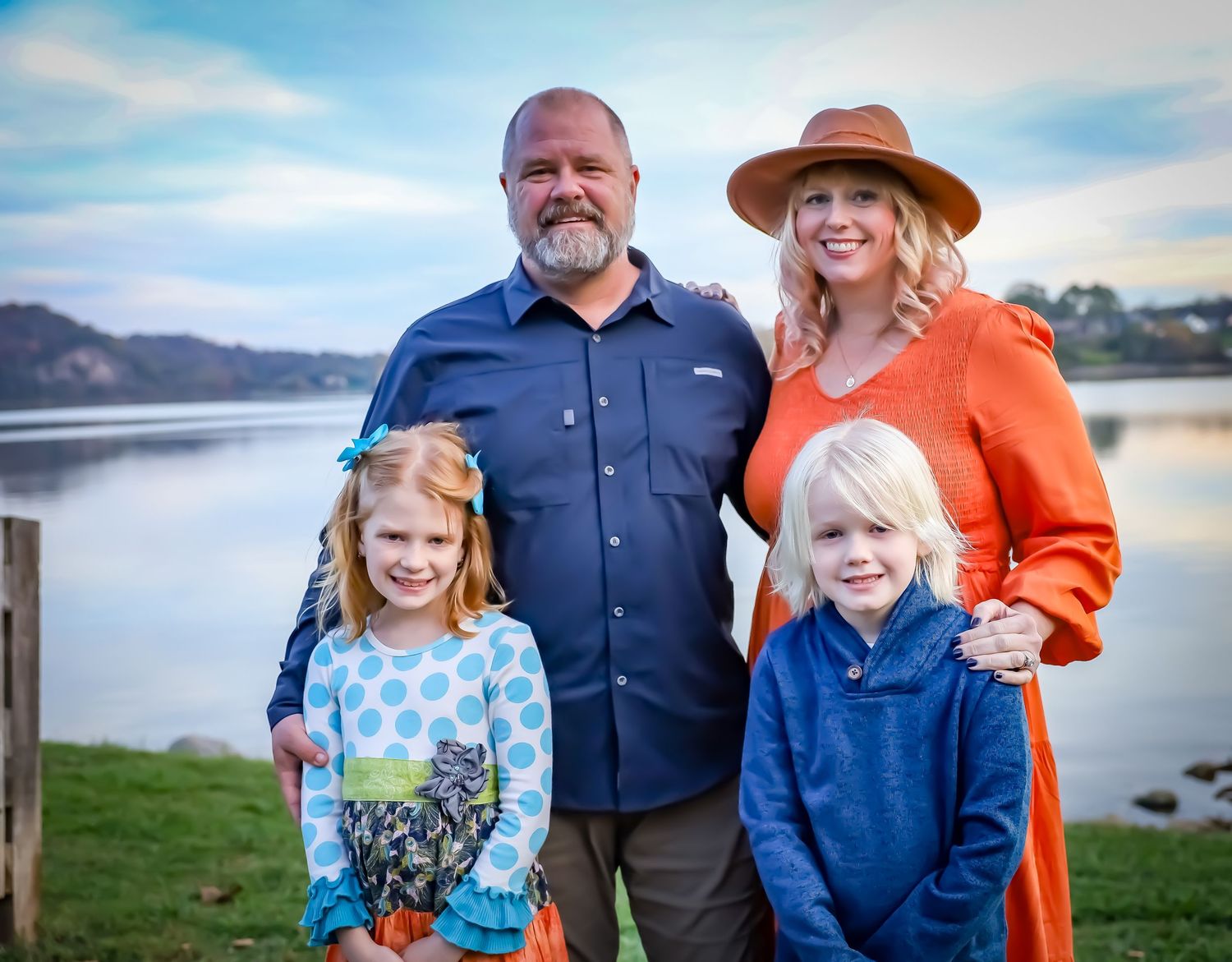 Family portrait session outdoors by a lake with mountains in the background.