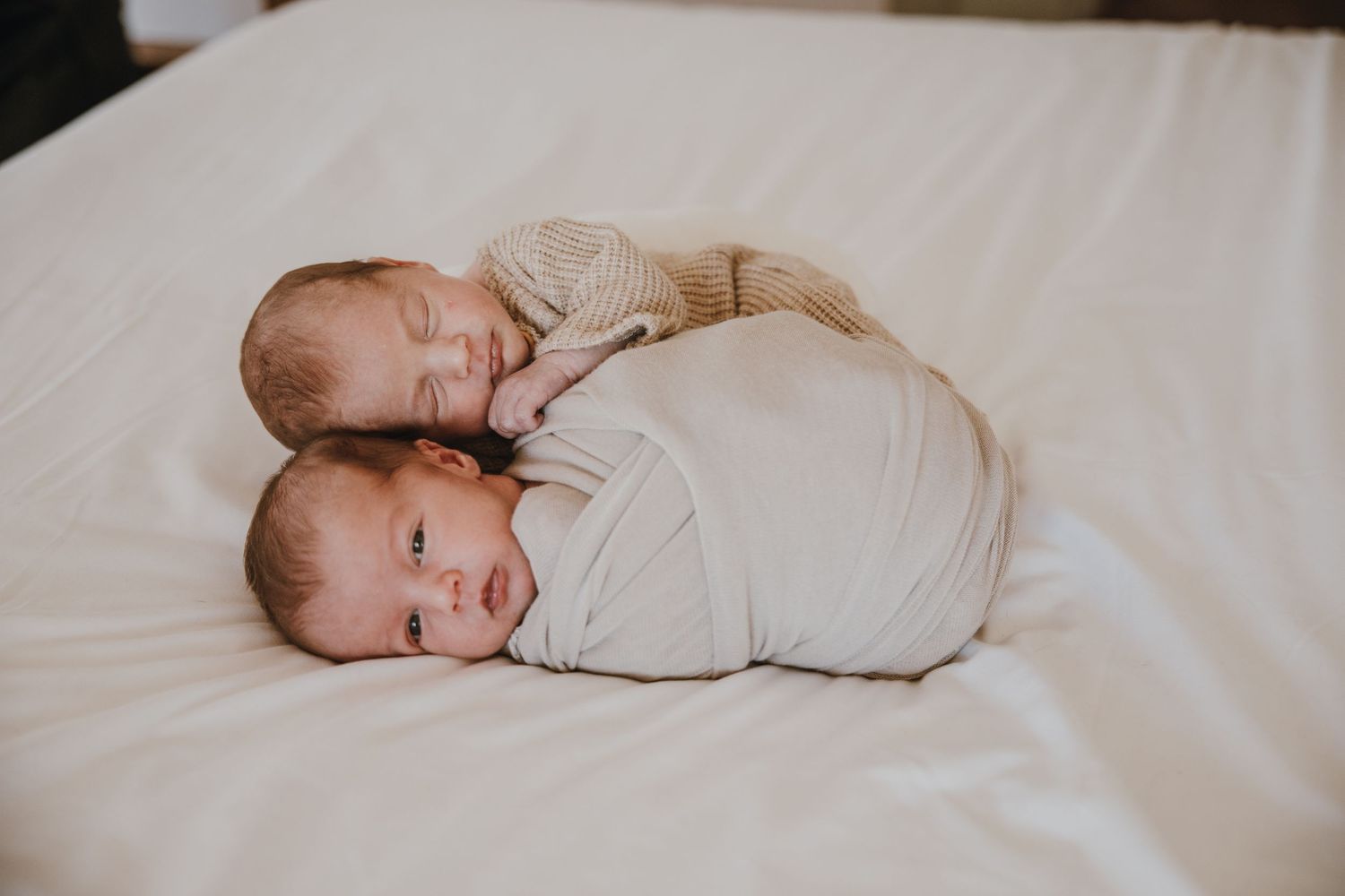 Two swaddled infants lay close together on white bedding.