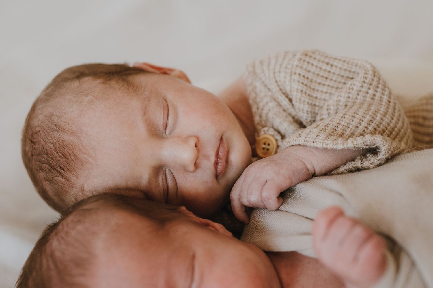 Twin babies sleeping peacefully together on white bedding.