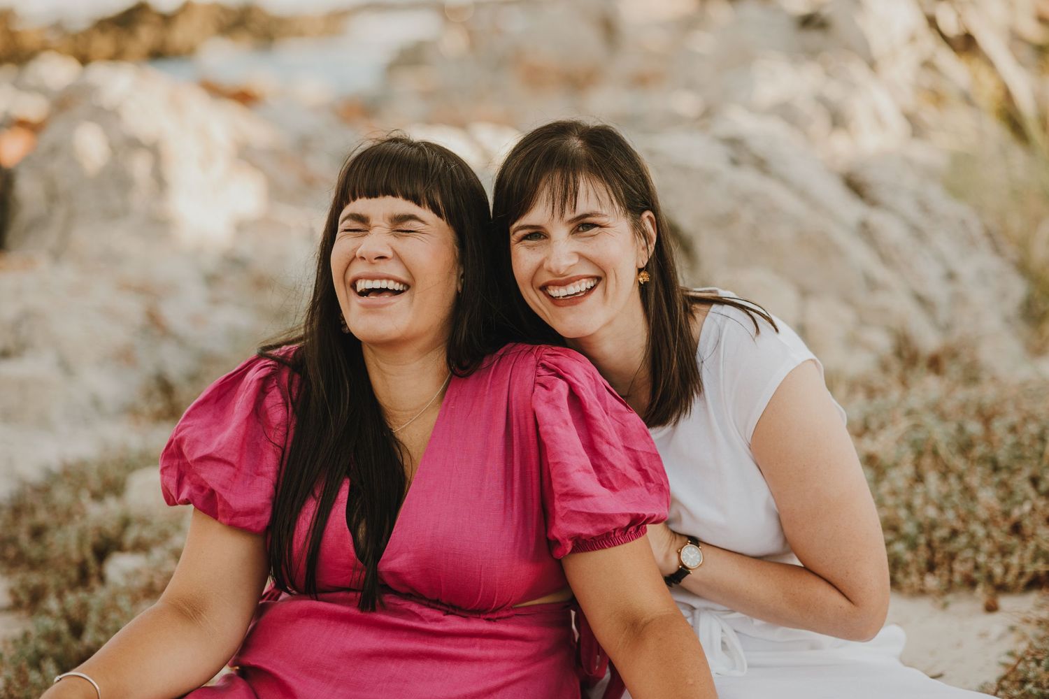 Two friends share genuine laughter while posing against rocky terrain.